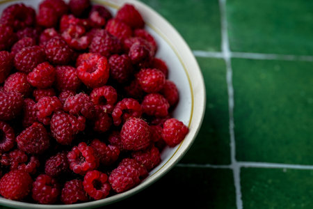 Plate of freshly picked red raspberries on green tile background. Concept of vibrant colors, summer,...