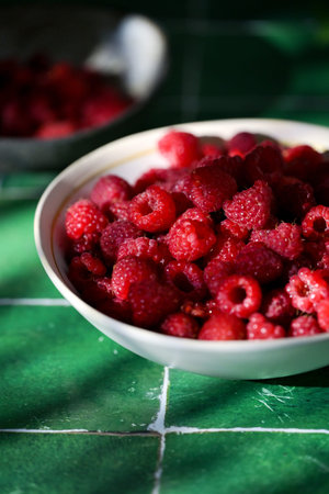 Plate of freshly picked red raspberries on green tile background. Concept of vibrant colors, summer,...