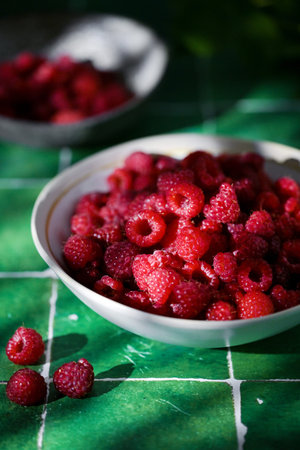 Plate of freshly picked red raspberries on green tile background. Concept of vibrant colors, summer,...