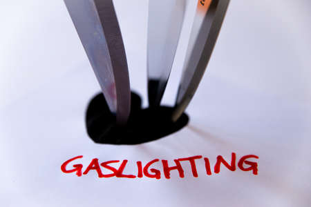 Word Gaslighting, written in red on white paper, next to black heart design, with knife bladesの写真素材
