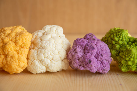 Cauliflower, yellow cauliflower, purple cauliflower and Roman cauliflower, placed next to each other, on a wooden surface.の写真素材