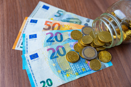 Savings, coins and banknotes on wooden surface and in a transparent jar. Money saved.の写真素材