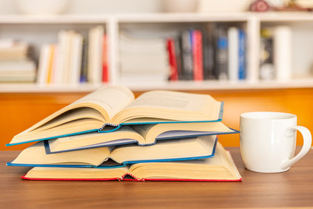 Open books, arranged one on top of the other, with a white cup of tea or coffee next to them, on a...