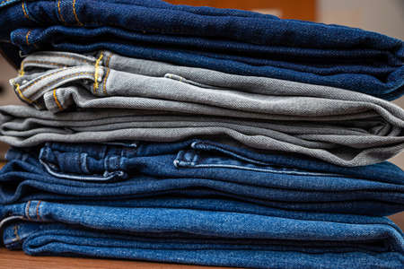 Folded jeans of various colors, arranged one on top of the other, and placed on a wooden surface.の写真素材