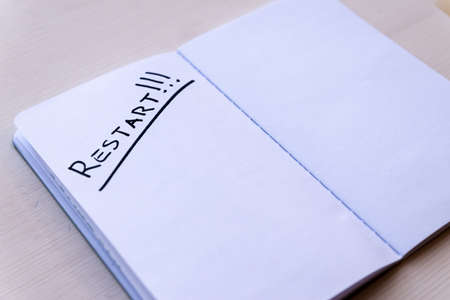 Restart! Starting again after a break, after a pandemic. Word "Restart" written in black ink on the blank page of a notebook, placed on a wooden surface.の写真素材