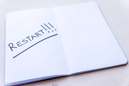 Restart! Starting again after a break, after a pandemic. Word "Restart" written in black ink on the blank page of a notebook, placed on a wooden surface.の写真素材