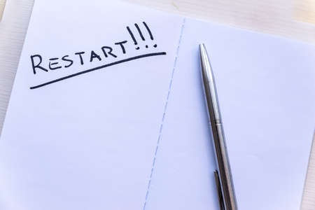 Restart! Starting again after a break, after a pandemic. Word "Restart" written in black ink on the blank page of a notebook, placed on a wooden surface.の写真素材