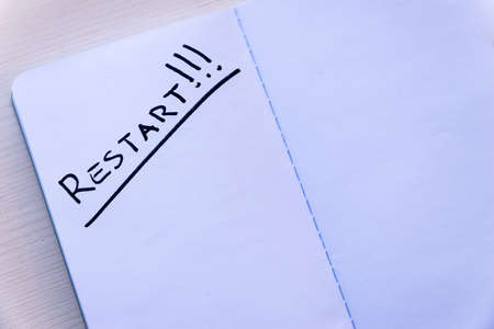 Restart! Starting again after a break, after a pandemic. Word "Restart" written in black ink on the blank page of a notebook, placed on a wooden surface.の写真素材