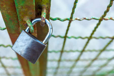 Dark colored padlock that closes a green gate. Protection of privacy and of one's own spaces. Closing.の写真素材