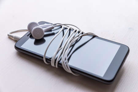 Smartphone with connected earphones, white in color. Earphone cord wrapped around the phone. Using earphones to listen to music or to make phone calls.の写真素材
