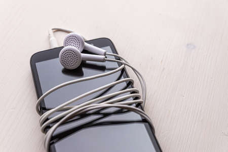 Smartphone with connected earphones, white in color. Earphone cord wrapped around the phone. Using earphones to listen to music or to make phone calls.の写真素材