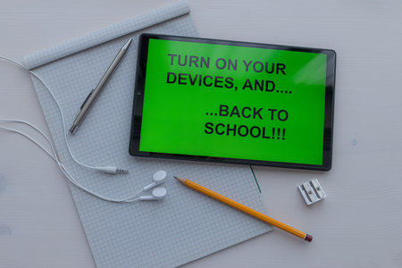 Tablet with text turn on your devices ... and back to school, on the screen, in black on a green...