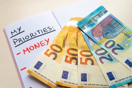 Blank diary page, with Priorities text in black ink; and text Money in red ink, with Euro banknotes...