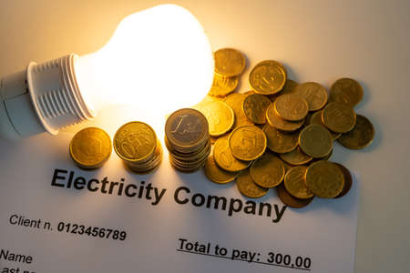Light bulb on, with banknotes, coins and energy bill. Increase in energy and gas tariffs. Efficiency and energy saving.の写真素材