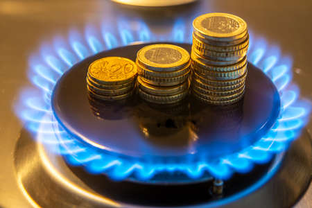 Gas stove lit, with stacks of coins above it. Increase in gas costs and tariffs.の写真素材