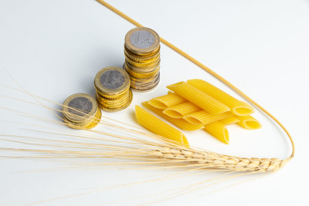 Ear of wheat, with pasta (pennette) and coins next to it. Increase in the price of wheat, pasta and...