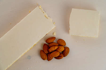 Pieces of hard nougat with almonds, with almonds next to it, on a light wooden surface.の写真素材