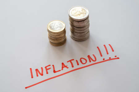 Stack of coins on white surface and red text "inflation". Rising prices and inflation.の写真素材