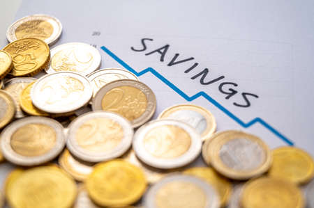 Graph with blue descending line, euro coins next to it, and black text "savings". Decrease in savings, and increase in prices and inflation.の写真素材