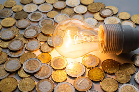 Light bulb turned on, with coins around. Increase in electricity tariffs, energy dependence, energy sources and energy supplies.の写真素材