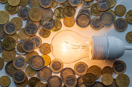 Light bulb turned on, with coins around. Increase in electricity tariffs, energy dependence, energy sources and energy supplies.の写真素材