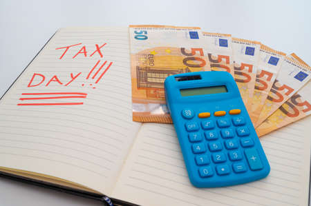 Page of diary with text "tax day", with banknotes and calculator next to it. Payment of taxes and tax deadlines.の写真素材
