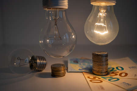 Light bulbs, one on and one off, above a pile of coins of increasing height. Increases in energy tariffs.の写真素材