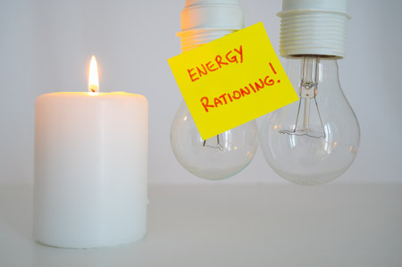 Lit candle, next to two unlit bulbs, with a yellow note with the text "energy rationing". Energy saving and rationing. Economic crisis.の写真素材