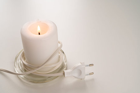 Lit candle, next to electric plug. Energy savings, increased tariffs and bills.