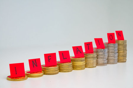 Stacks of coins, and on top of them red tickets spelling the word inflation. Rising inflation and...