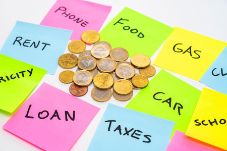 Coins on a white surface, with colored sticker sheets next to them, with expense items.