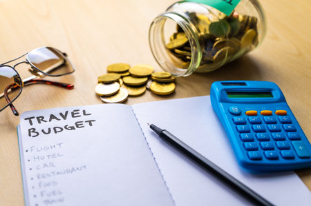 Notebook with the words travel budget and coins in the glass jarの写真素材