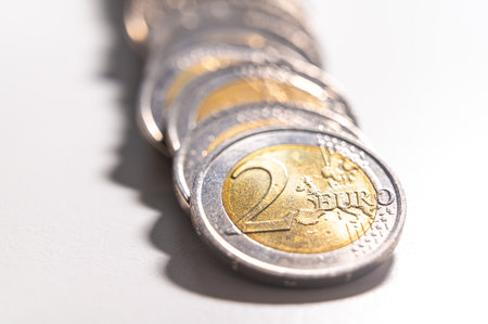 Rows of coins on a white surface, photographed against light and shadow.の写真素材