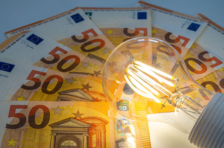 Light bulb lit, above euro banknotes. Electricity costs and tariffs.の写真素材