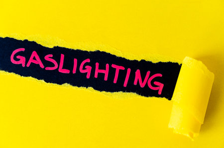 Black surface, with word gaslighting in red. Underneath torn yellow cardboard.の写真素材