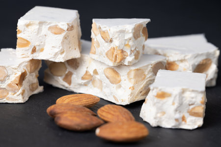 Pieces of hard nougat, with almonds next to it, on a dark slate surface.の写真素材