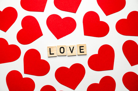 Word Love, composed with wooden squares, next to red hearts, on a white surface.