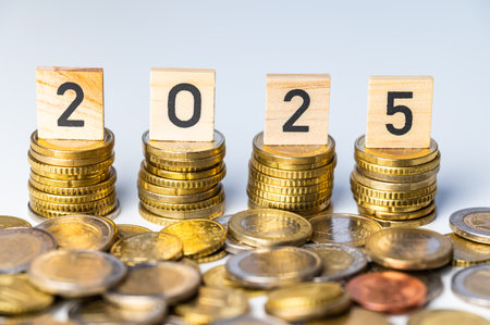 Piles of coins, and wooden cubes that spell out the number 2025. New year, economy and wealth.の写真素材
