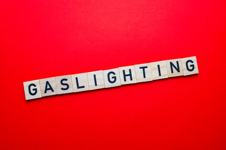 Word Gaslighting, written with wooden alphabet blocks, on red surface.の写真素材