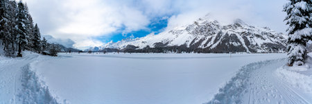 Panorama of Lake Sils, in Engadine, Switzerland, frozen and snowy, and the mountains above.
