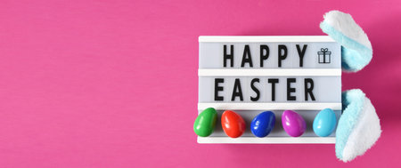 Wide banner with inscription Happy Easter with colored eggs and bunny white and blue ears on purple...