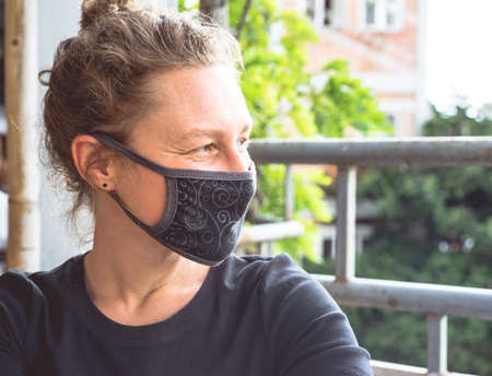 New normal fashion look, a very happy smiling young Caucasian girl puts on black medical protection face mask and looks right, virus and pollution safety measures, social distancing and stop the covidの写真素材