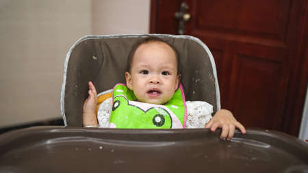 Qingyuan, China - April 22, 2017: little dirty baby in a feeding chair after eating porridge, dirty child's face after the food, funny a cute toddler sits in a high chair for infants, soft focusのeditorial素材