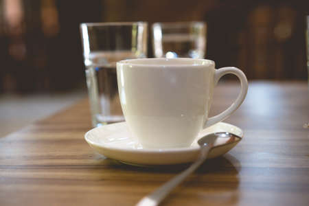 white cup of coffee on the table and two glass of water, cup of tea in a white cup with spoon at the cafe, soft focusの写真素材