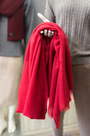 clothes in a shop, red cashmere scarf in a showroom, clothing store, woollen products, mannequin exposing elegant classic cloth, piece of red textile in a handの写真素材