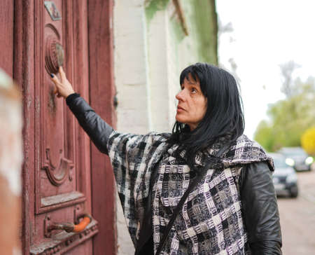 A beautiful adult woman at the front of the door, travelling in Europe, old rustic door in the abandoned house, a person knocking on the door to come in.の写真素材