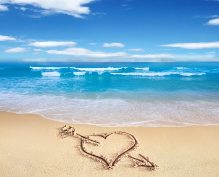 Heart with arrow, as love sign, drawn on the beach shore, with the see and sky in the background.の写真素材
