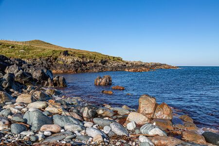 A rocky beach on the Hebridean island of North Uist, with a clear blue sky overheadの写真素材