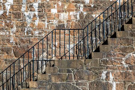 An outside staircase with metal railings against a stone wallの写真素材