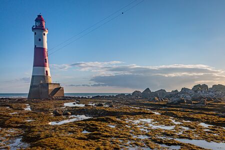 Beachy Head Lighthouse at low tide as seen from the beach, with a blue sky overheadの写真素材